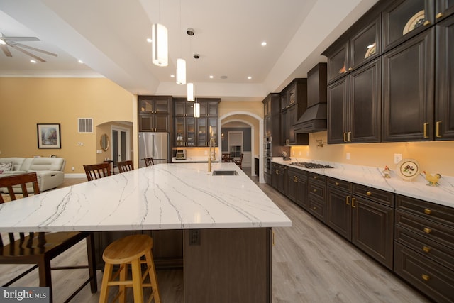 kitchen featuring arched walkways, hanging light fixtures, appliances with stainless steel finishes, glass insert cabinets, and a large island with sink