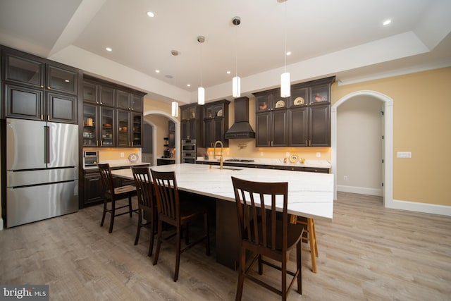 kitchen with arched walkways, a large island, stainless steel appliances, premium range hood, and pendant lighting