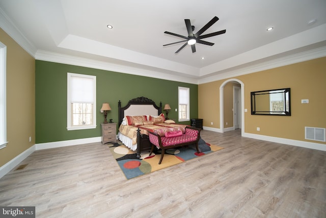 bedroom with arched walkways, visible vents, baseboards, light wood-style floors, and a tray ceiling