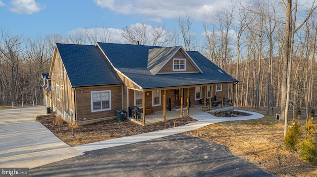 view of front facade featuring a porch, a shingled roof, and a forest view