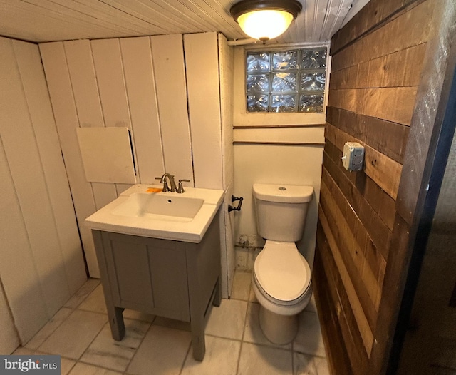 bathroom with vanity, toilet, and wood walls