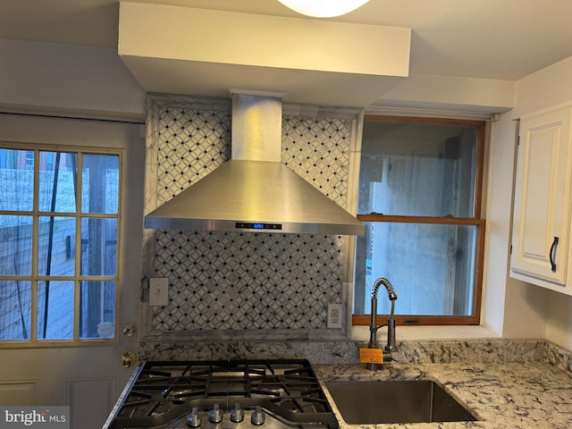 kitchen with tasteful backsplash, white cabinetry, light stone countertops, and wall chimney range hood