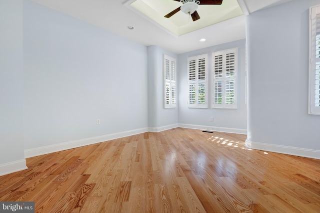 unfurnished room with ceiling fan, a tray ceiling, and light hardwood / wood-style flooring