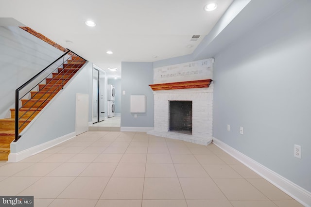 unfurnished living room featuring a brick fireplace, light tile patterned floors, and stacked washer and clothes dryer