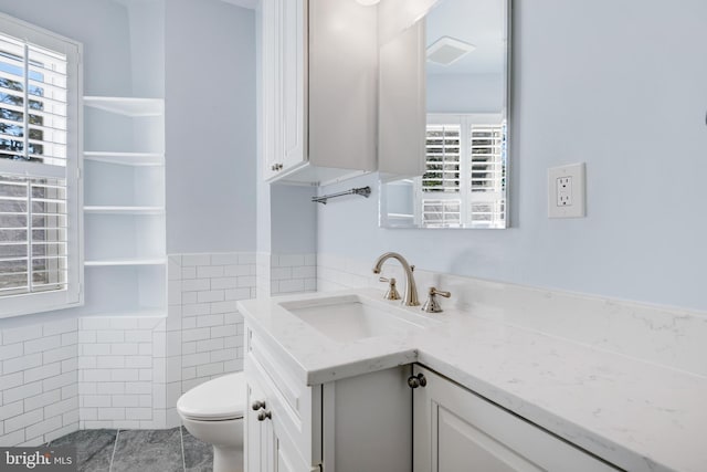 bathroom featuring vanity, toilet, and tile walls