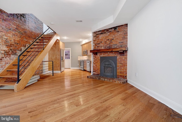 unfurnished living room with brick wall, a fireplace, and light hardwood / wood-style floors