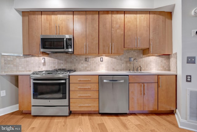 kitchen featuring decorative backsplash, stainless steel appliances, sink, and light hardwood / wood-style flooring