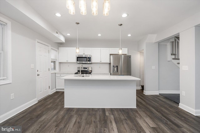 kitchen featuring pendant lighting, dark wood-type flooring, appliances with stainless steel finishes, an island with sink, and white cabinets