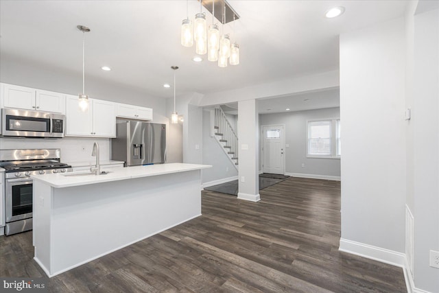 kitchen featuring sink, pendant lighting, stainless steel appliances, a kitchen island with sink, and white cabinets