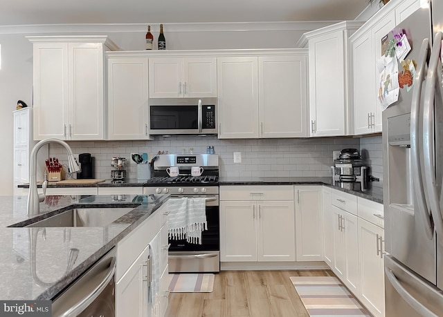 kitchen with sink, white cabinetry, dark stone countertops, stainless steel appliances, and light hardwood / wood-style floors