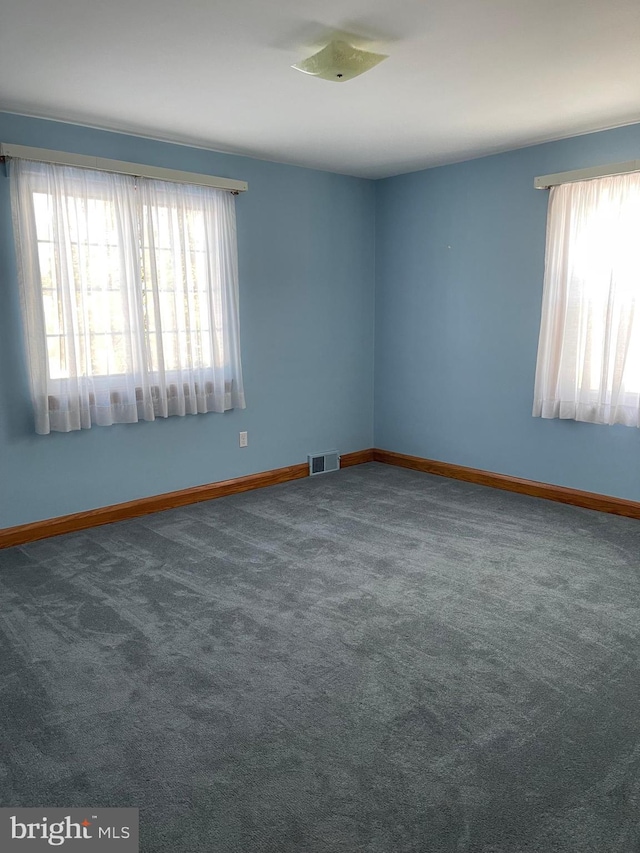 unfurnished room with plenty of natural light and dark carpet