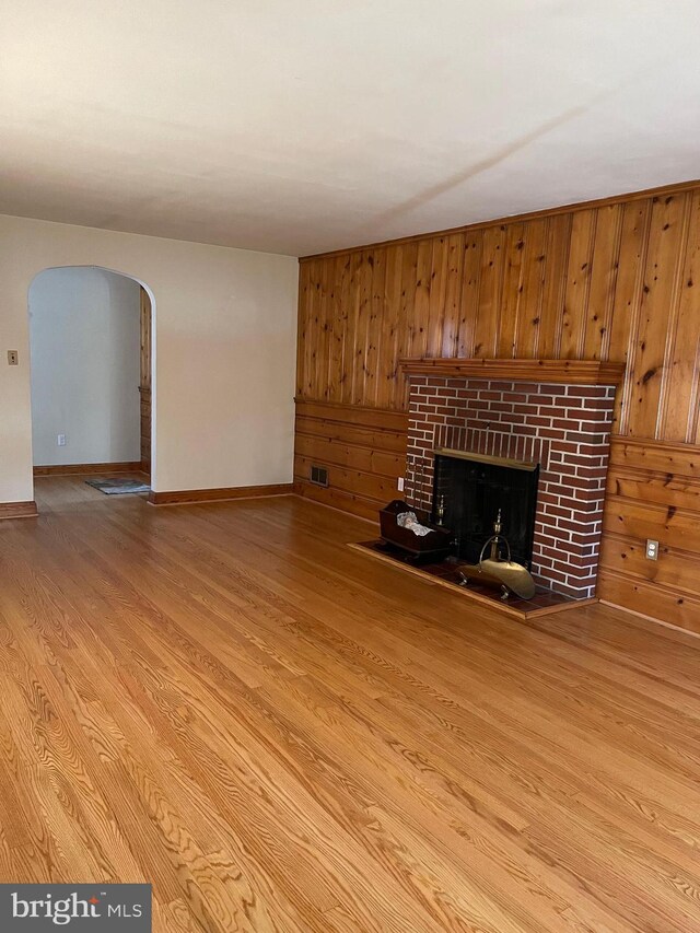 unfurnished living room featuring wood walls, a brick fireplace, and light wood-type flooring