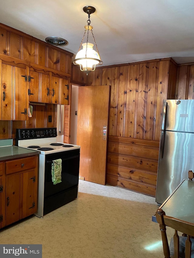 kitchen with light carpet, electric range oven, stainless steel refrigerator, wooden walls, and pendant lighting