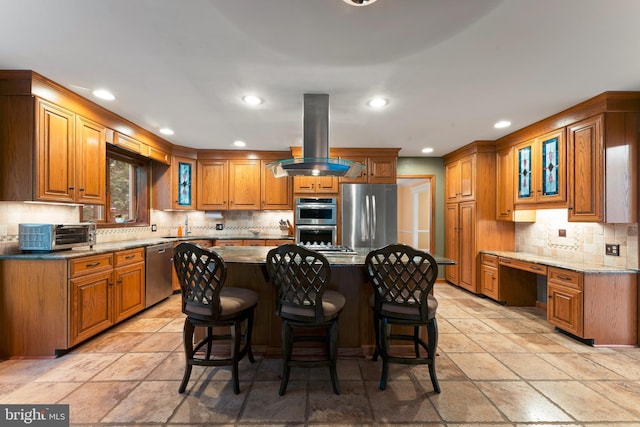 kitchen featuring appliances with stainless steel finishes, a kitchen breakfast bar, island range hood, built in desk, and a kitchen island