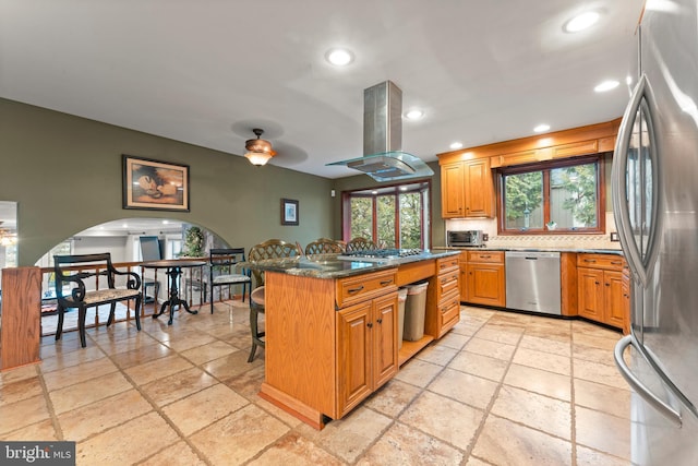 kitchen featuring appliances with stainless steel finishes, island range hood, a kitchen breakfast bar, dark stone counters, and a center island