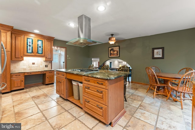 kitchen featuring a center island, island range hood, stainless steel gas cooktop, decorative backsplash, and dark stone counters