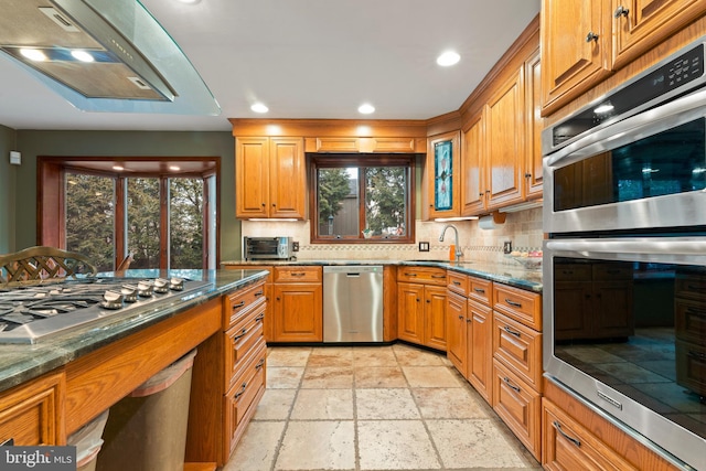 kitchen with appliances with stainless steel finishes, sink, backsplash, and dark stone counters