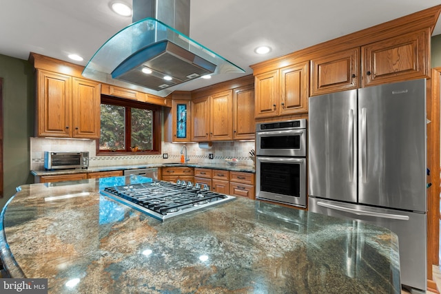 kitchen featuring sink, tasteful backsplash, dark stone countertops, island exhaust hood, and stainless steel appliances