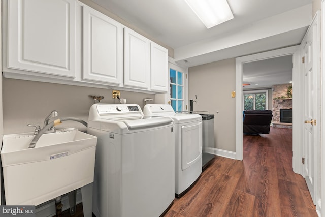 laundry room featuring a stone fireplace, sink, cabinets, dark hardwood / wood-style floors, and washing machine and dryer