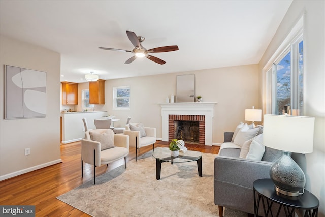 living area featuring ceiling fan, a fireplace, baseboards, and wood finished floors