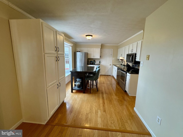 kitchen featuring sink, appliances with stainless steel finishes, ornamental molding, light hardwood / wood-style floors, and white cabinets