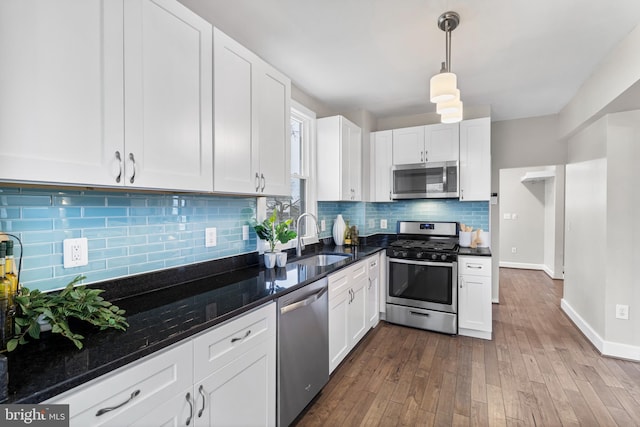 kitchen with dark wood-style floors, stainless steel appliances, white cabinets, a sink, and pendant lighting