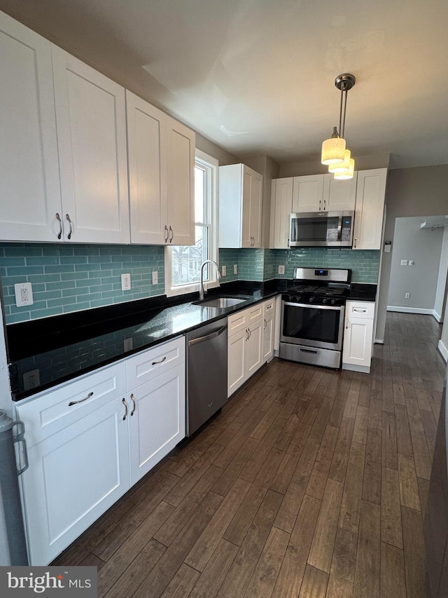 kitchen with a sink, dark countertops, pendant lighting, white cabinetry, and stainless steel appliances