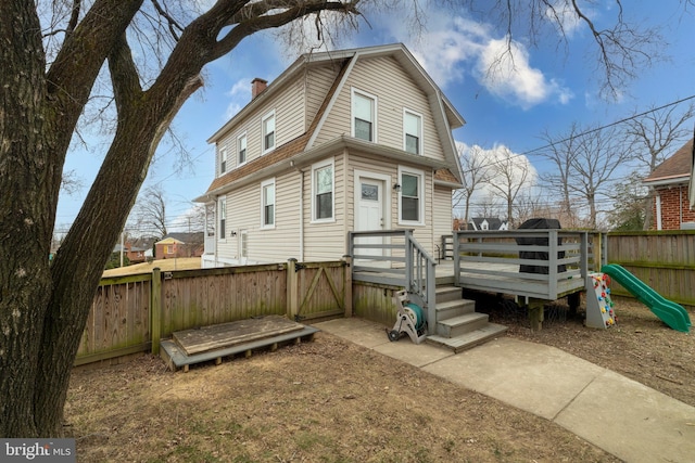 back of house with a gate, a wooden deck, a chimney, a gambrel roof, and a fenced backyard