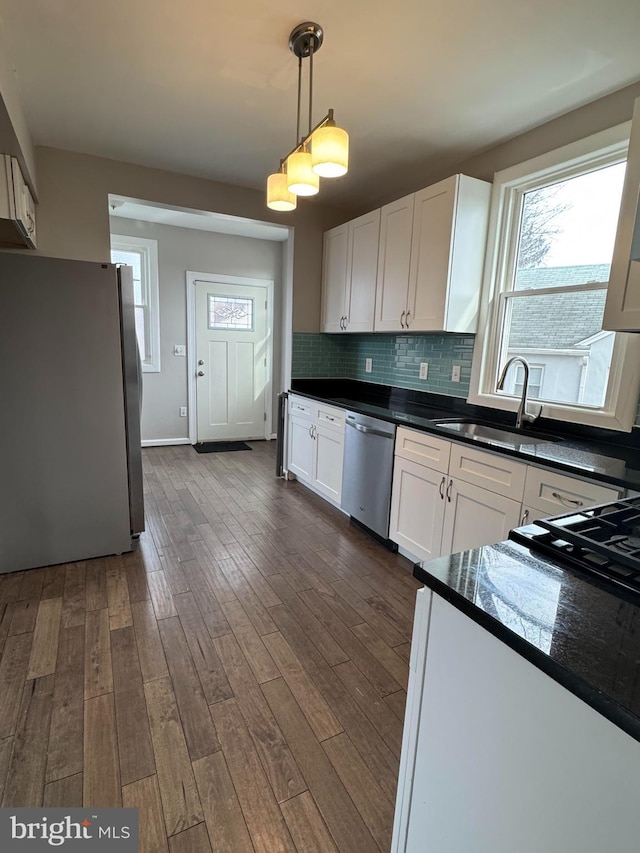 kitchen with dark countertops, tasteful backsplash, appliances with stainless steel finishes, white cabinets, and pendant lighting