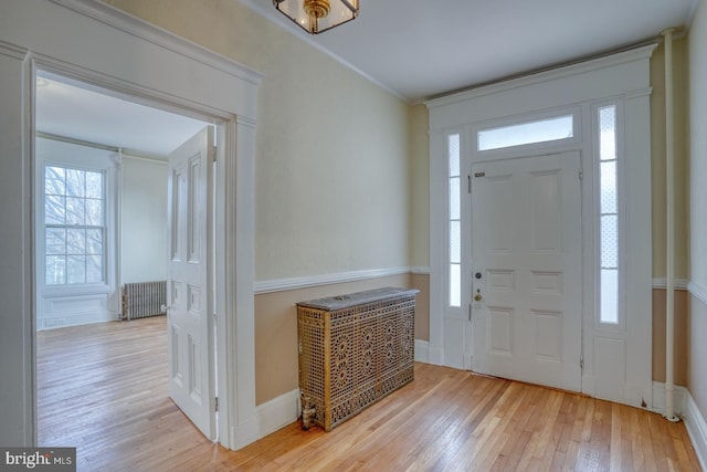 foyer entrance with radiator, crown molding, and light hardwood / wood-style floors