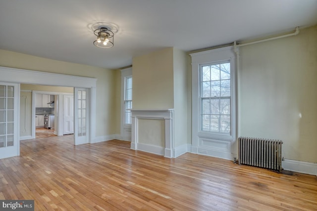 unfurnished living room featuring radiator, light hardwood / wood-style floors, and french doors