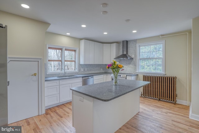 kitchen with sink, radiator heating unit, white cabinets, and wall chimney exhaust hood