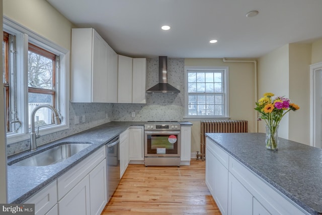 kitchen featuring wall chimney exhaust hood, sink, white cabinetry, light wood-type flooring, and stainless steel appliances