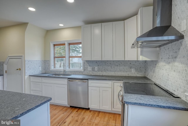 kitchen with wall chimney range hood, sink, light hardwood / wood-style flooring, white cabinetry, and stainless steel appliances