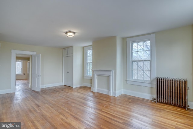 unfurnished living room with radiator, a fireplace, and light wood-type flooring