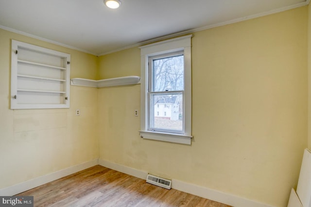 empty room featuring crown molding, built in features, and light hardwood / wood-style flooring