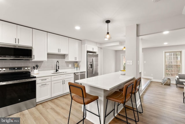 kitchen with sink, appliances with stainless steel finishes, white cabinetry, hanging light fixtures, and a kitchen breakfast bar