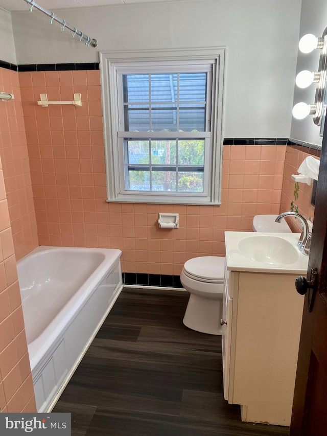 bathroom featuring hardwood / wood-style floors, tile walls, vanity, a washtub, and toilet