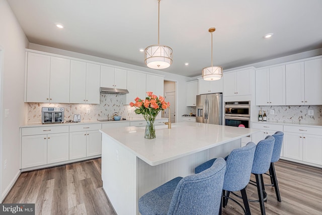 kitchen featuring white cabinetry, stainless steel appliances, an island with sink, and hanging light fixtures