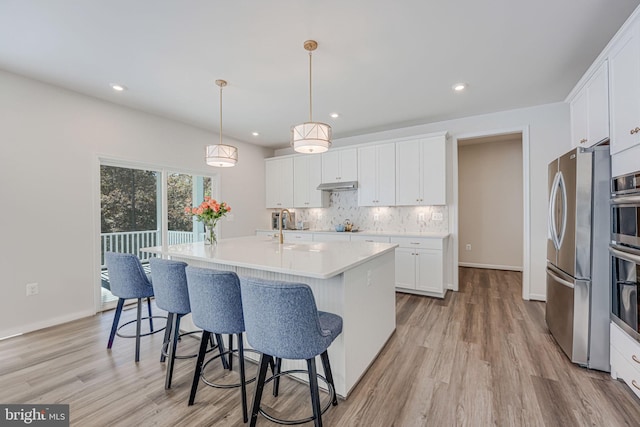 kitchen with sink, backsplash, an island with sink, white cabinets, and decorative light fixtures