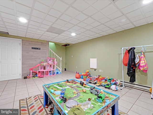 rec room with tile patterned flooring, a baseboard radiator, a drop ceiling, and wooden walls