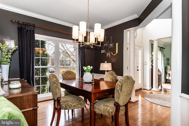 dining space with hardwood / wood-style flooring, ornamental molding, a chandelier, and decorative columns