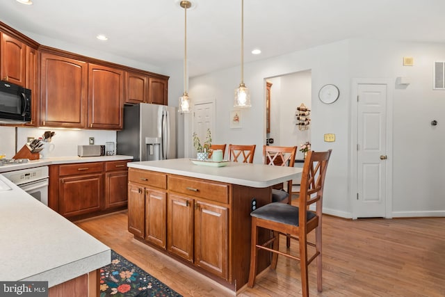 kitchen with a kitchen island, a kitchen breakfast bar, hanging light fixtures, white appliances, and light wood-type flooring