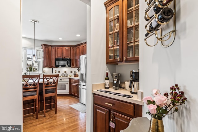 kitchen featuring light wood-type flooring, hanging light fixtures, stainless steel fridge, and white oven