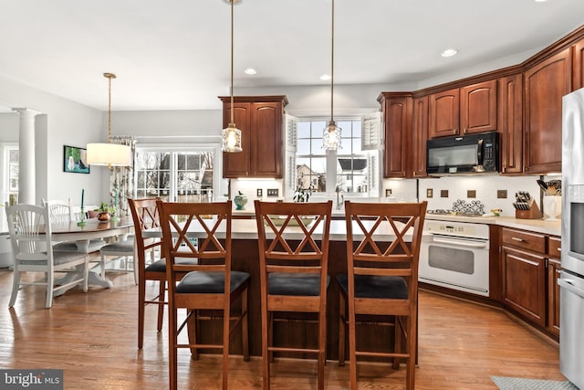 kitchen featuring hanging light fixtures, white appliances, a center island, and a kitchen bar