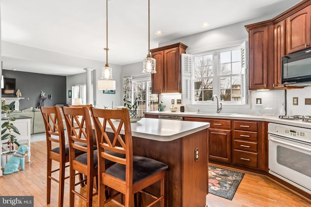 kitchen with white appliances, decorative light fixtures, a breakfast bar, and a kitchen island