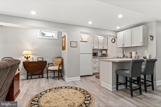 kitchen featuring white cabinetry, light wood-type flooring, a breakfast bar area, and white fridge