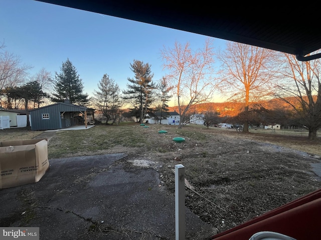 yard at dusk featuring a carport and an outdoor structure