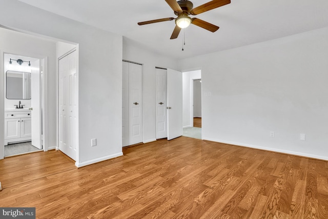 unfurnished bedroom with sink, ensuite bath, light hardwood / wood-style floors, and multiple closets