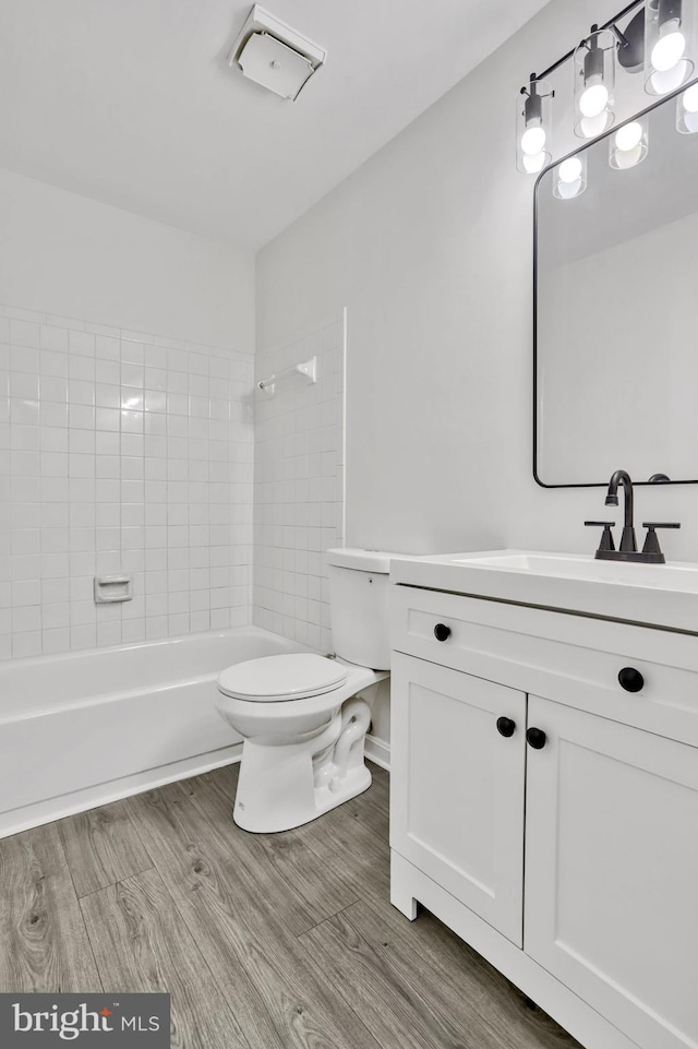 full bathroom with vanity, tiled shower / bath, hardwood / wood-style floors, and toilet